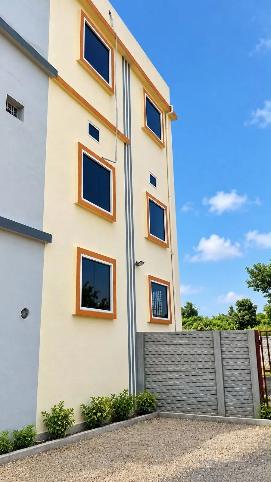 Tall three-level home with a yellow facade, orange-framed windows and a compound wall in Anuppur